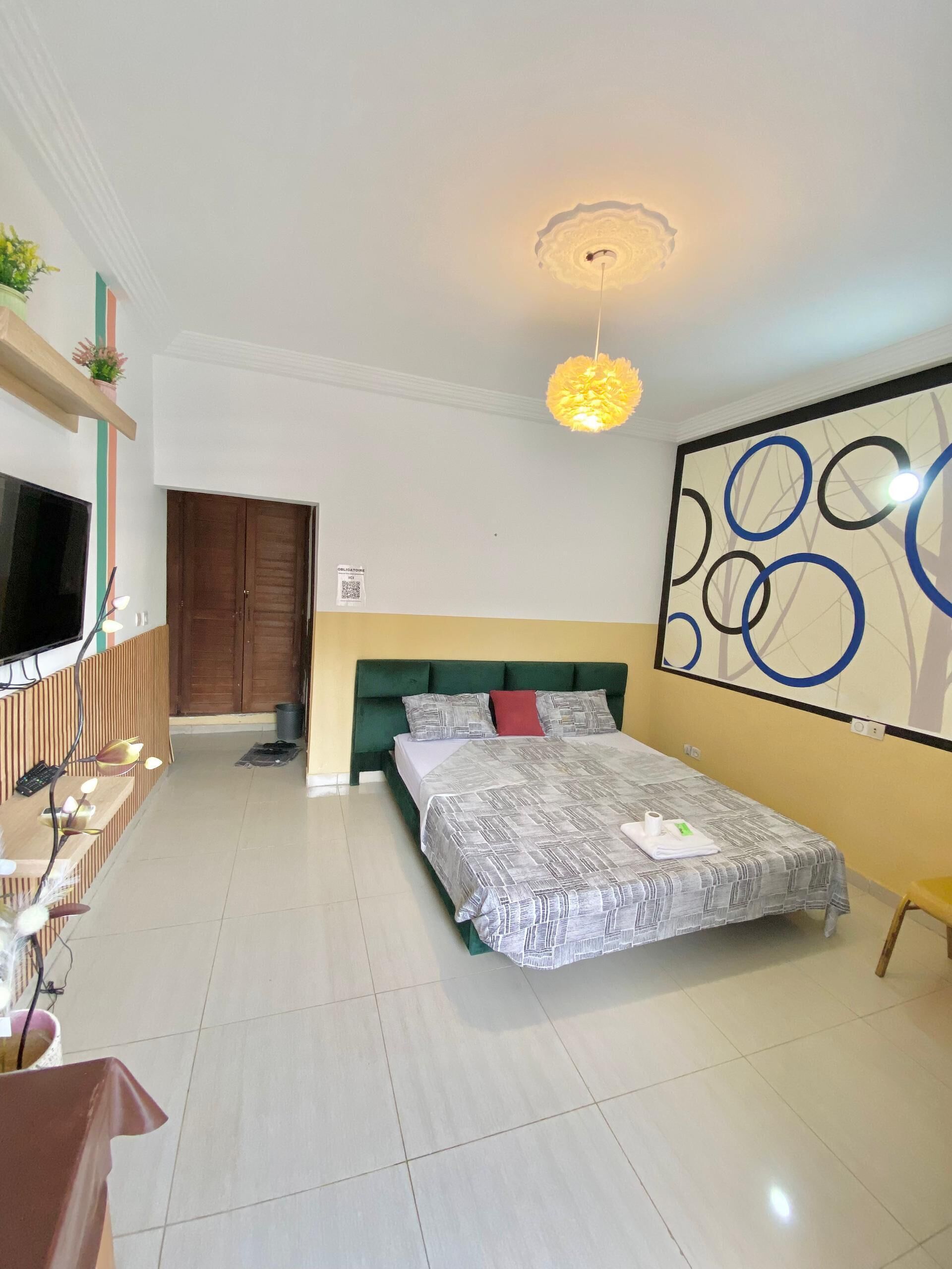 Een hotelkamer met een bed, een televisie, een bureau en een muur met abstracte kunst.