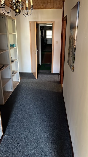 Un pasillo con piso alfombrado, una puerta de madera, una pared blanca y un candelabro.