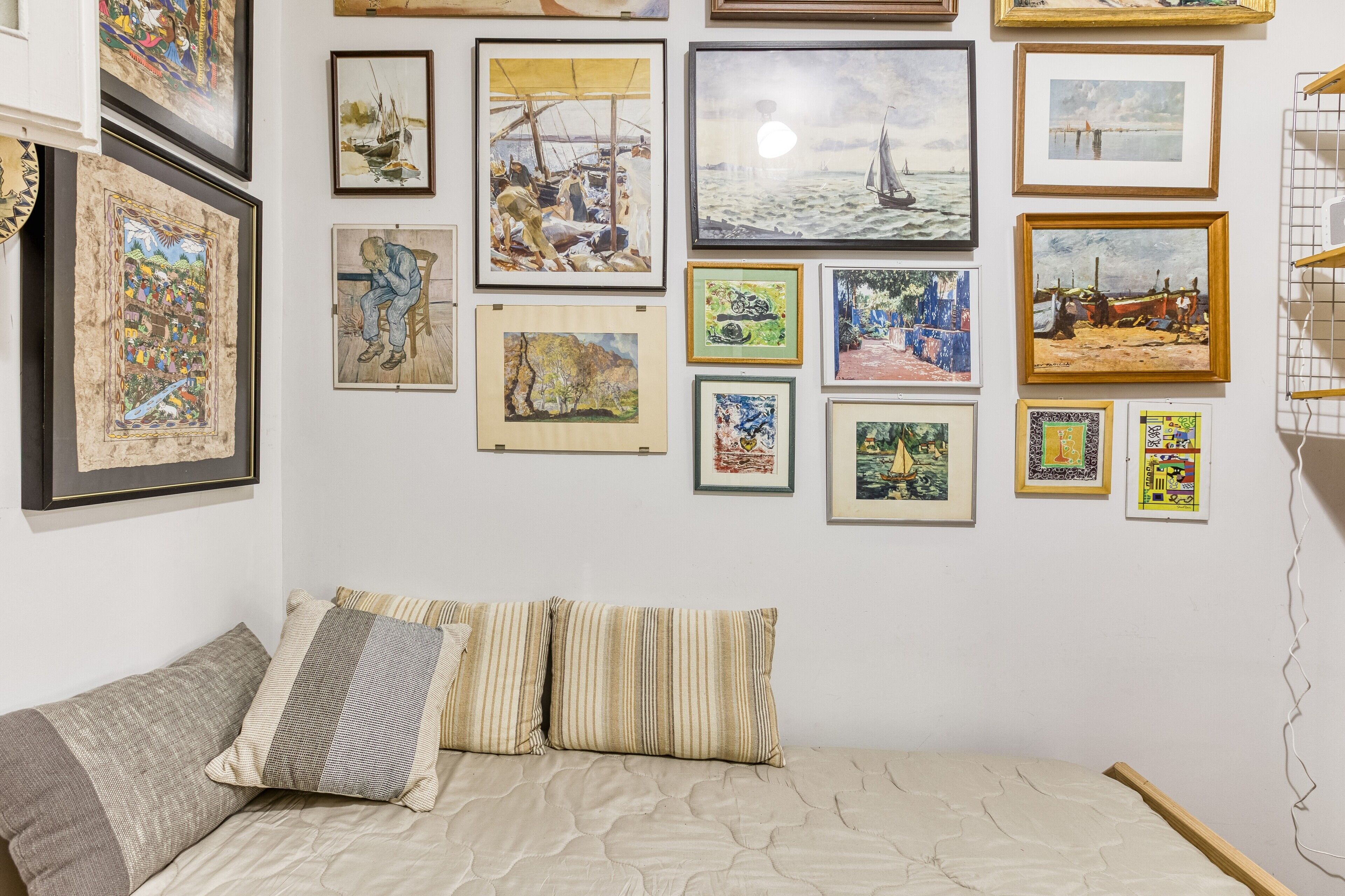 Ein Zimmer mit einem Bett, Kissen und einer Wand, die mit verschiedenen gerahmten Kunstwerken geschmückt ist.