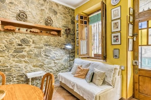 Un mur en pierre, des meubles en bois, un canapé avec des coussins, une table à manger et une fenêtre avec des rideaux.