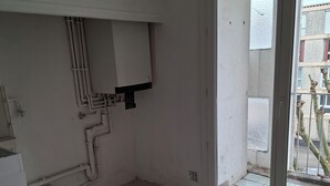 Ein Zimmer mit Fliesenboden, einer Tür zu einem Außenbereich und sichtbarer Sanitärinstallation an der Wand.