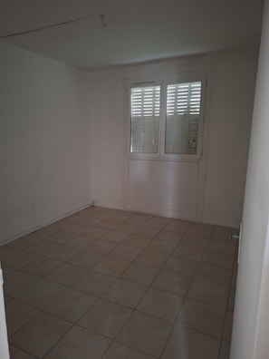 Ein Zimmer mit Fliesenboden, einer Tür mit Fenster und einer weißen Wand.