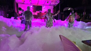 Un palco con sfondo illuminato di rosa e casse acustiche, circondato da schiuma.