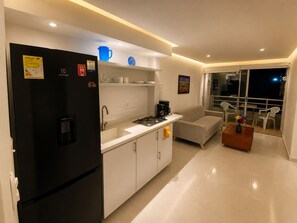 Eine moderne Küche mit einem schwarzen Kühlschrank, weißen Schränken, einem Gasherd und einem Spülbecken. Im Wohnbereich befindet sich eine Couch und ein kleiner Tisch mit einer Vase.