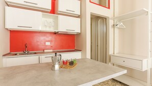 Une cuisine avec des meubles blancs, un crédence rouge, une machine à café et un étendoir suspendu.