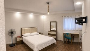 Une chambre à coucher comprenant un lit, une table de chevet, un miroir, un bureau, une chaise et un téléviseur fixé au mur.