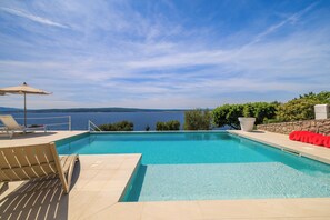 Ein Schwimmbecken mit Meerblick, Liegestühlen und einer Steinmauer.