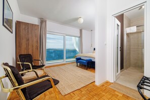 Ein modernes Hotelzimmer mit großem Fenster, einem Bett, einem Sessel und einem kleinen Tisch.