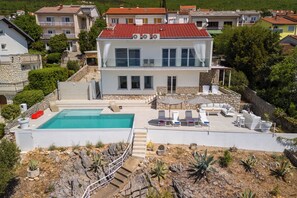 Ein zweistöckiges Haus mit Swimmingpool, Sitzgelegenheiten im Freien und einer Steinmauer.