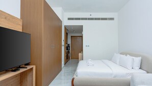 A modern hotel room with a flat-screen TV, wooden wardrobe, a bed with white linens, and a small seating area. - Modern Studio with Premium Amenities (Dubai)