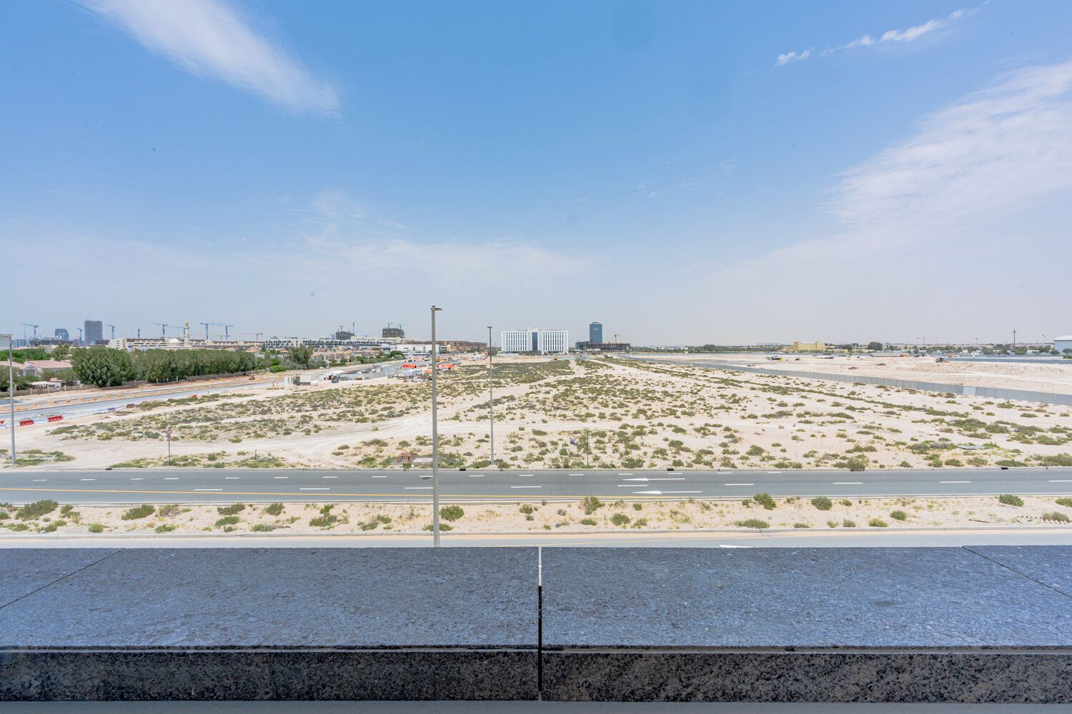 A desert landscape with a road, buildings, and construction cranes in the distance.