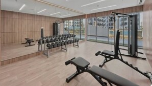 A modern gym with weightlifting equipment, mirrored walls, and large windows. - Modern Studio with Premium Amenities (Dubai)