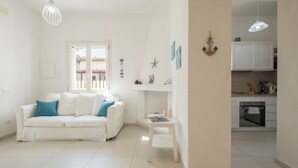Una sala de estar blanca con un sofá blanco, una mesita pequeña y una cocina con armarios y una estufa blancos.