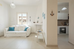 A white living room with a white sofa, a small white table, and a kitchen area with white cabinets and a stove. - [Stunning Villa]private garden-front beach-parking [Smart TV Wi-Fi] (Solanas)