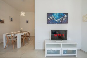 A modern living room with a dining area, a flat-screen TV, and a wall-mounted artwork. - [Stunning Villa]private garden-front beach-parking [Smart TV Wi-Fi] (Solanas)
