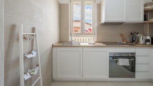 Una cocina con armarios blancos, horno de acero inoxidable, pileta y ventana con vista a edificios.