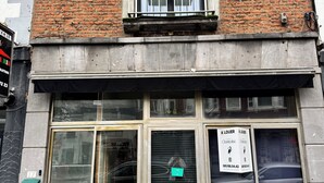 En bygning med murstensfacade, et vindue med balkon og en butik med skilt.