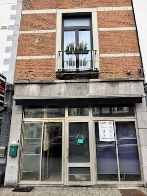 A building with a brick facade, a window with a balcony, and a storefront with a sign. - Duplex next to the Casino de Namur (Namur)