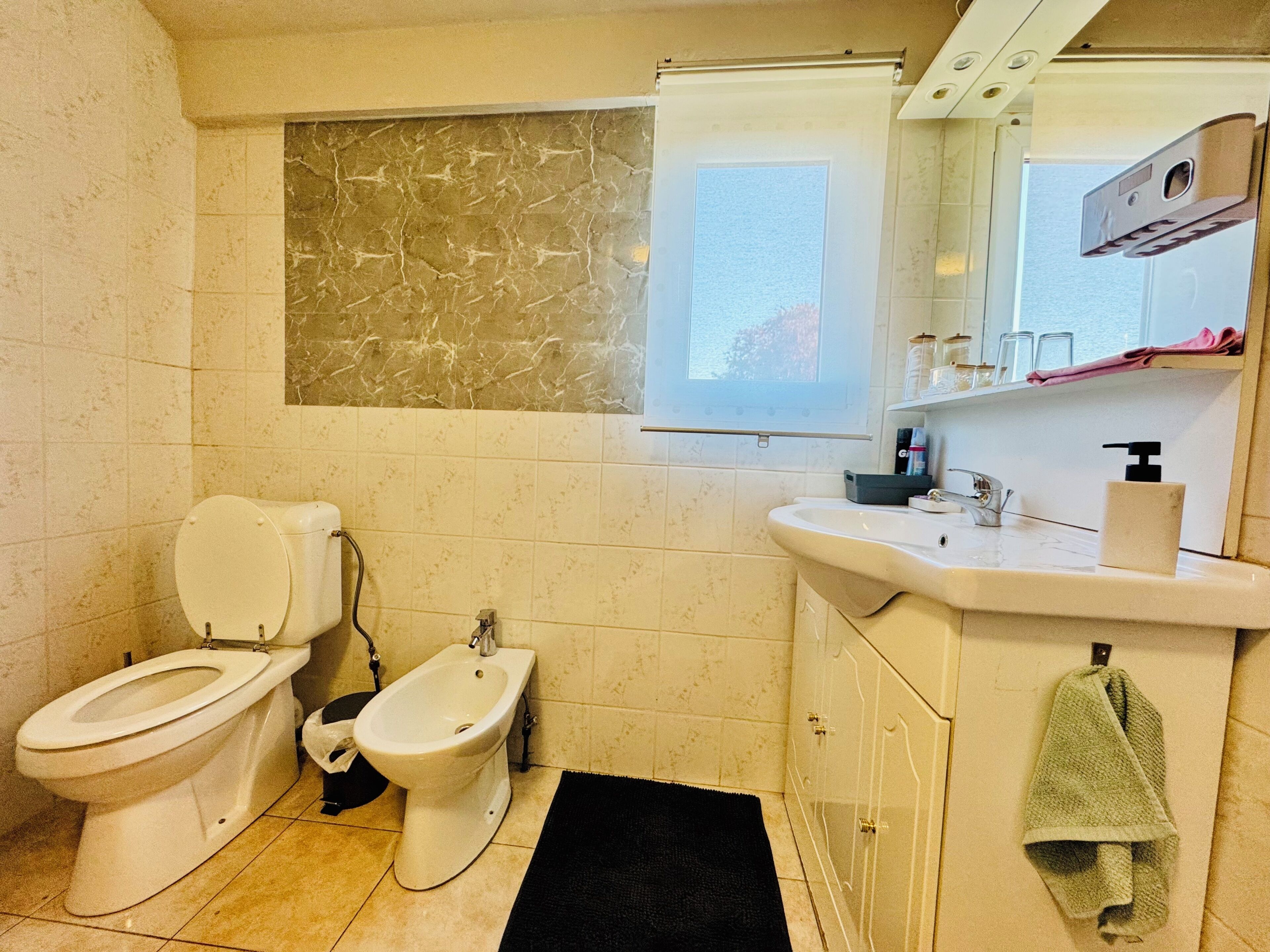 Un baño con inodoro, bidé, lavamanos y ventana.