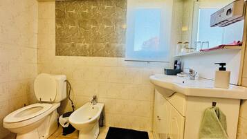 Un baño con inodoro, bidé, lavamanos y ventana.