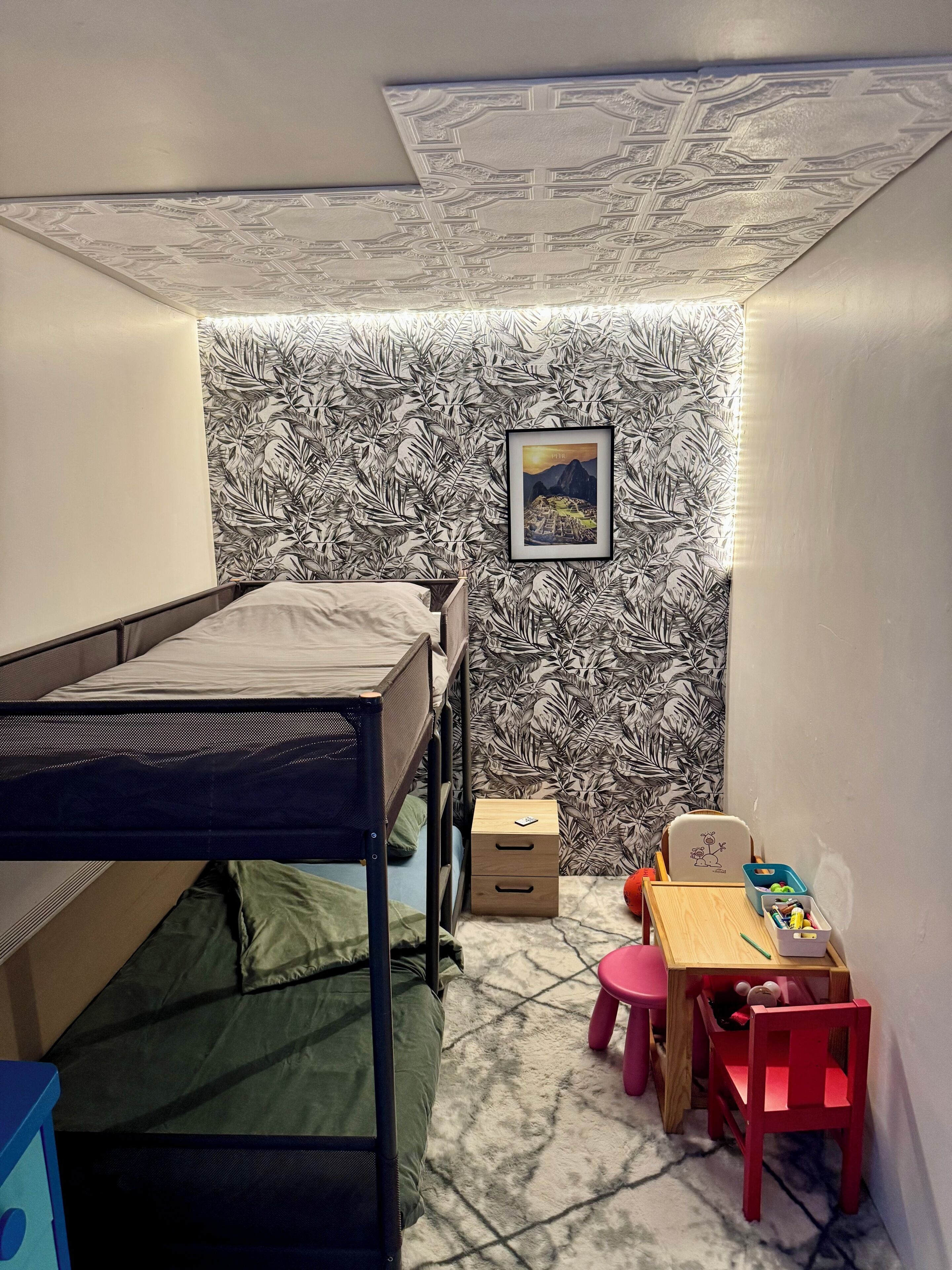 Een slaapkamer met een stapelbed, een bureau met stoel, een klein krukje en een ingelijste foto aan de muur.