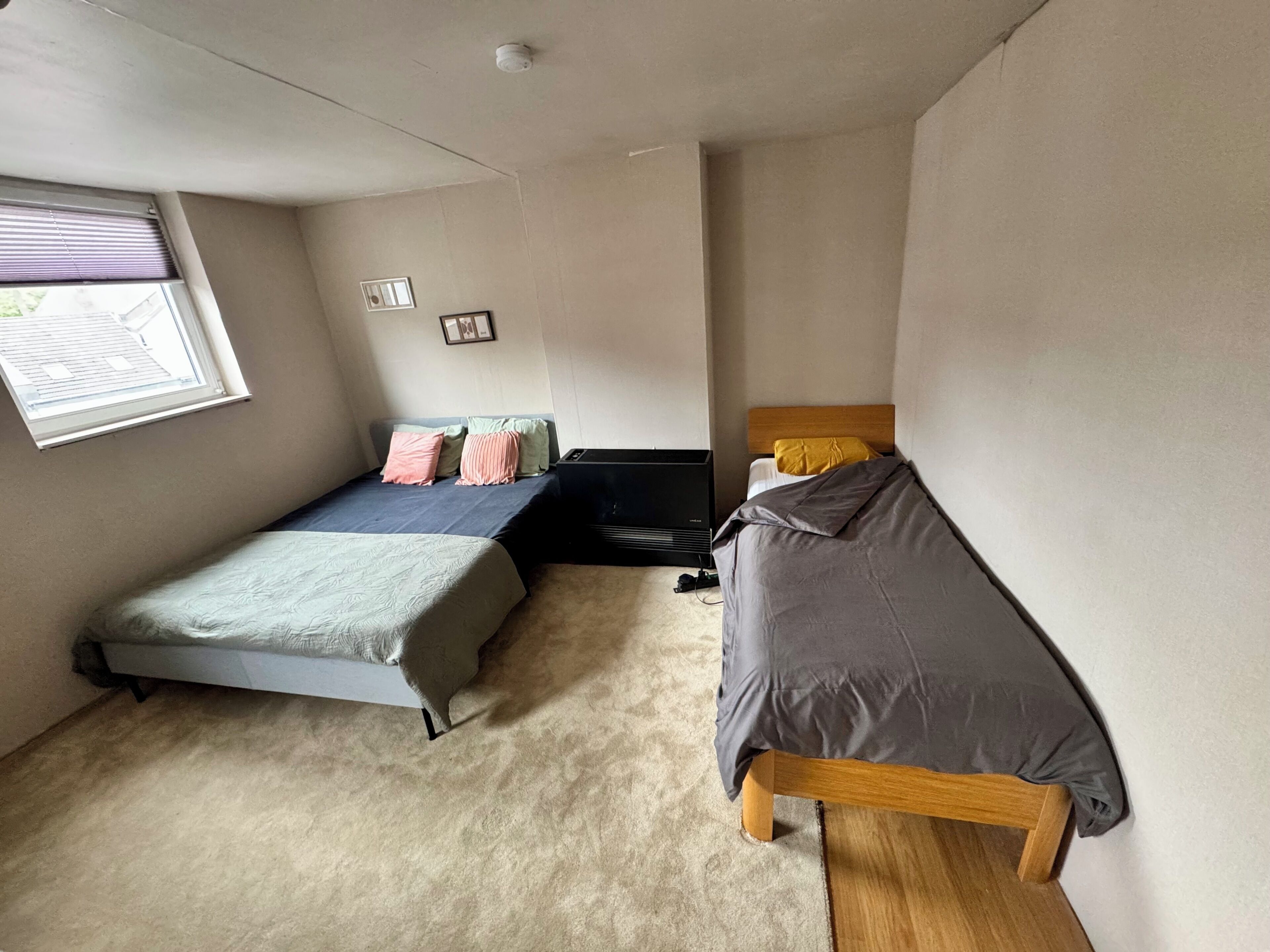 Une petite chambre avec un lit simple, une fenêtre, un radiateur et un banc en bois.