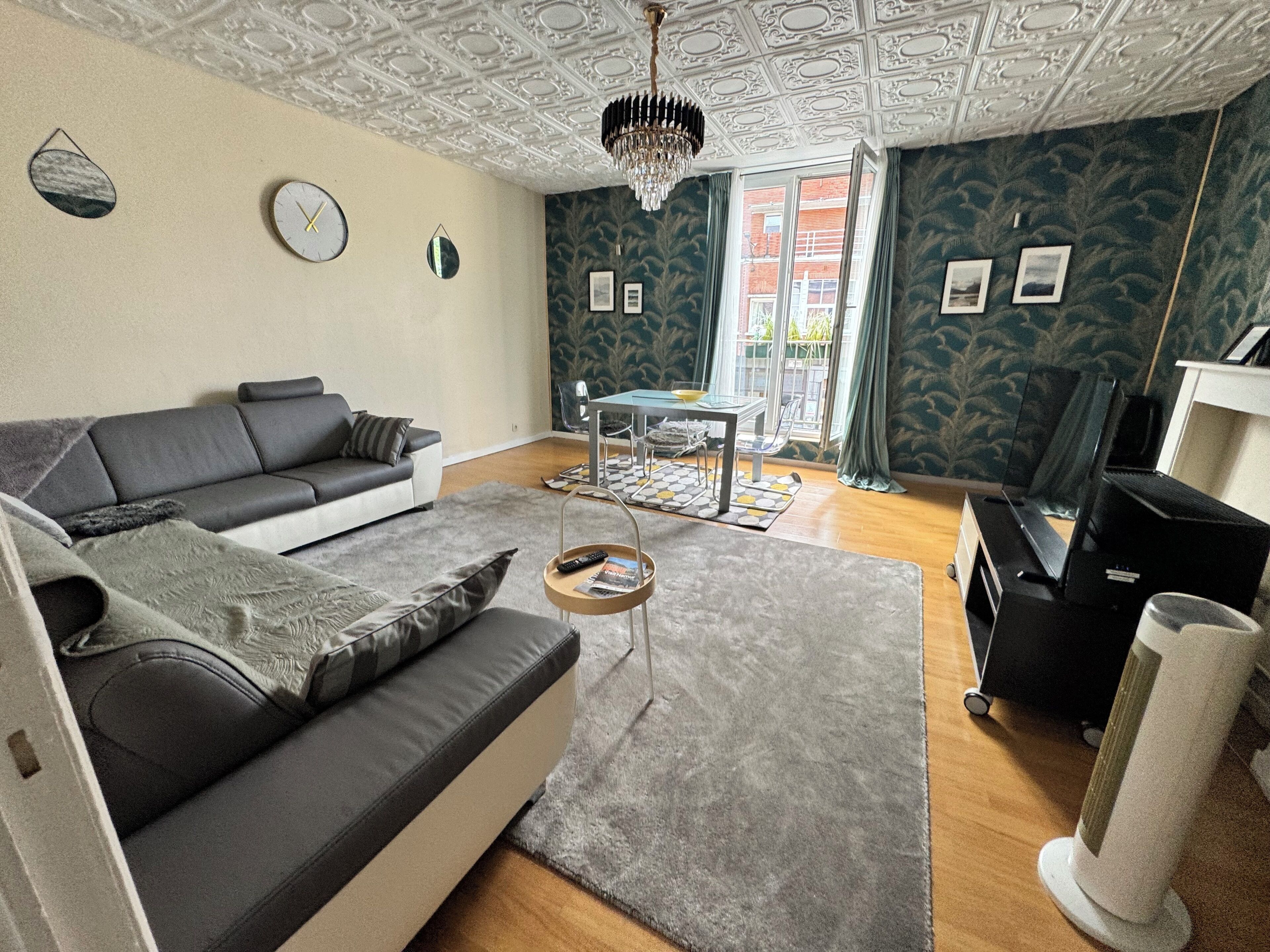 A living room with a sofa, a coffee table, a chandelier, and a view of the outside.
