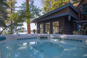 Ein Whirlpool mit einer Holzhütte im Hintergrund, umgeben von Bäumen und einem See.