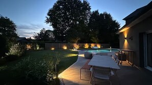 A backyard with a pool, outdoor seating, and a large tree.