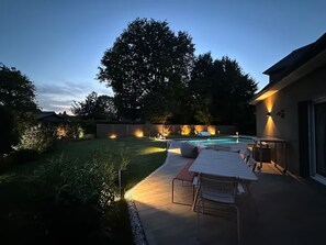 A backyard with a pool, outdoor seating, and a large tree.