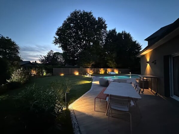A backyard with a pool, outdoor seating, and a large tree.