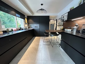 A modern kitchen with a central island, bar stools, a built-in oven, and a large window.