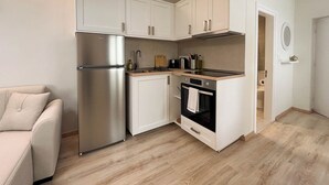 A compact kitchen with white cabinets, a stainless steel refrigerator, a black oven, and a wooden countertop. - Kumquat Apartments (Corfu)