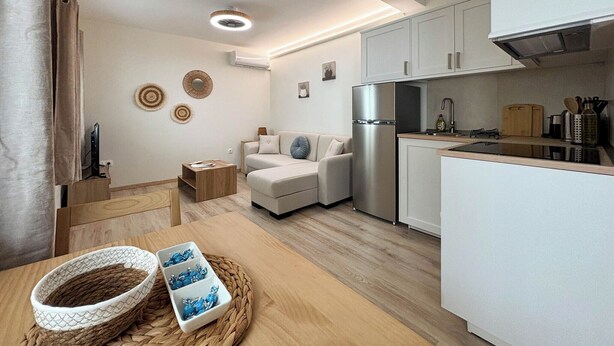 A compact living space with a kitchenette, a sofa, a dining table, and decorative wall art. - Kumquat Apartments (Corfu)