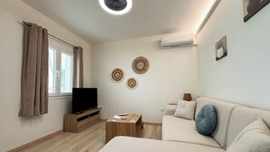 A living room with a sofa, a TV on a wooden stand, a small table, and a ceiling light. - Kumquat Apartments (Corfu)