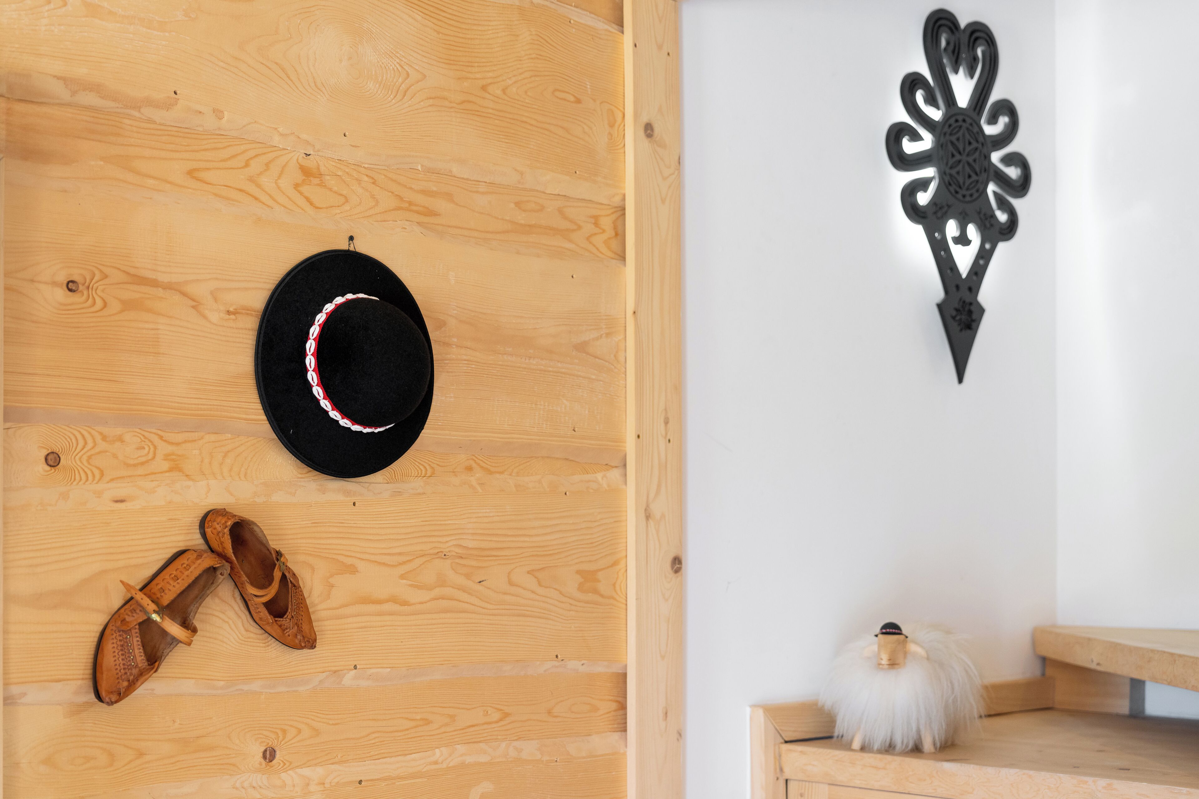 A wooden wall with a hat and shoes, a decorative wall piece, and a small white object on a shelf.