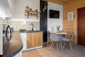 A modern kitchen with a wooden island, a dining area with a round table and chairs, and a mounted deer head on the wall. - RentPlanet Góralski Domek w Chochołowie (Chochołów)
