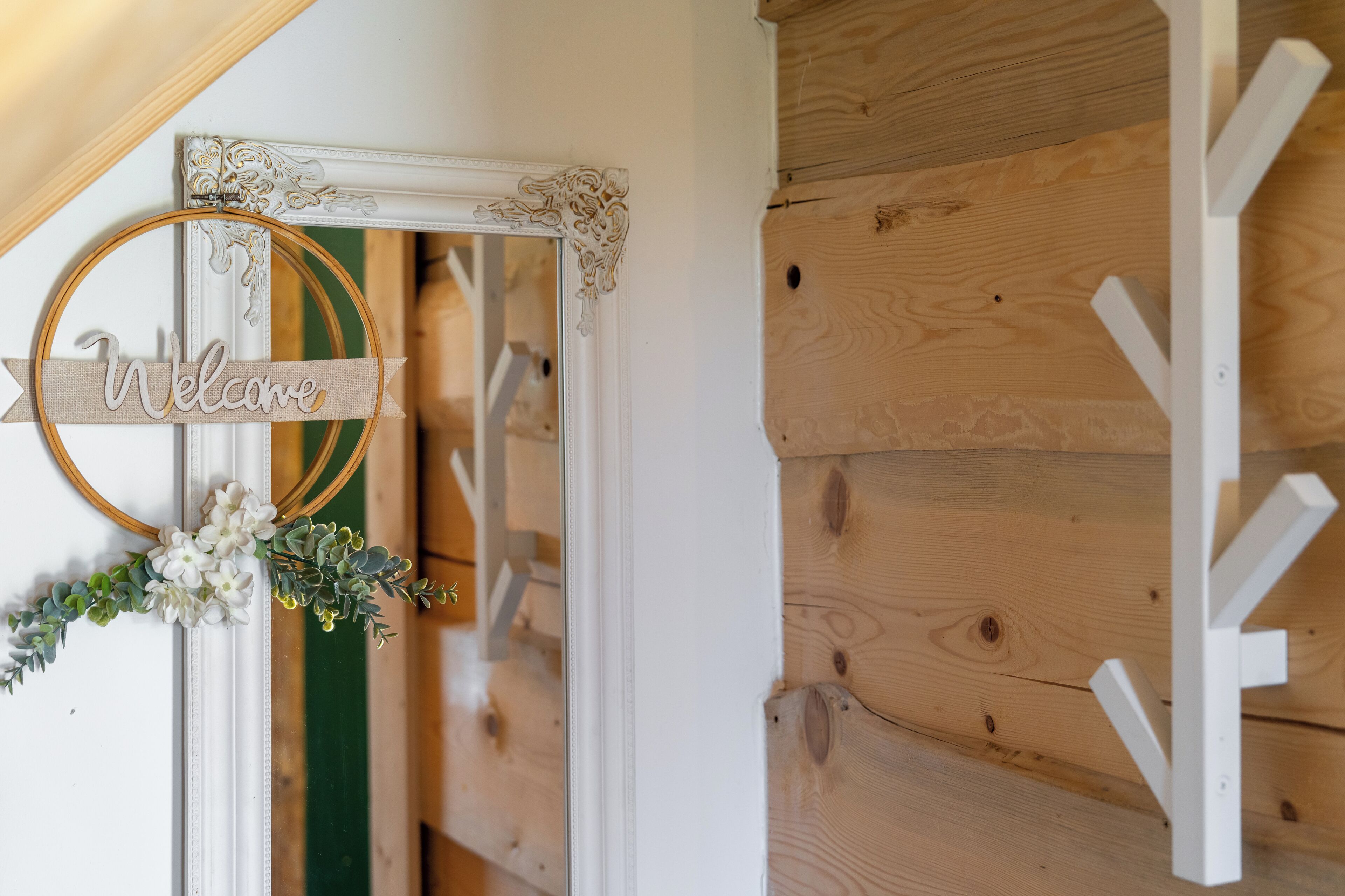 A wooden wall with a white door, a white mirror with a 'Welcome' sign, and a white light fixture.