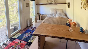 Un dormitorio con cama, una mesa de madera, un tapete colorido y vistas al exterior.