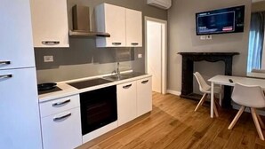 A modern kitchen with white cabinets, a built-in oven, and a dining area with a table and chairs. - HH Tortona (Tortona)