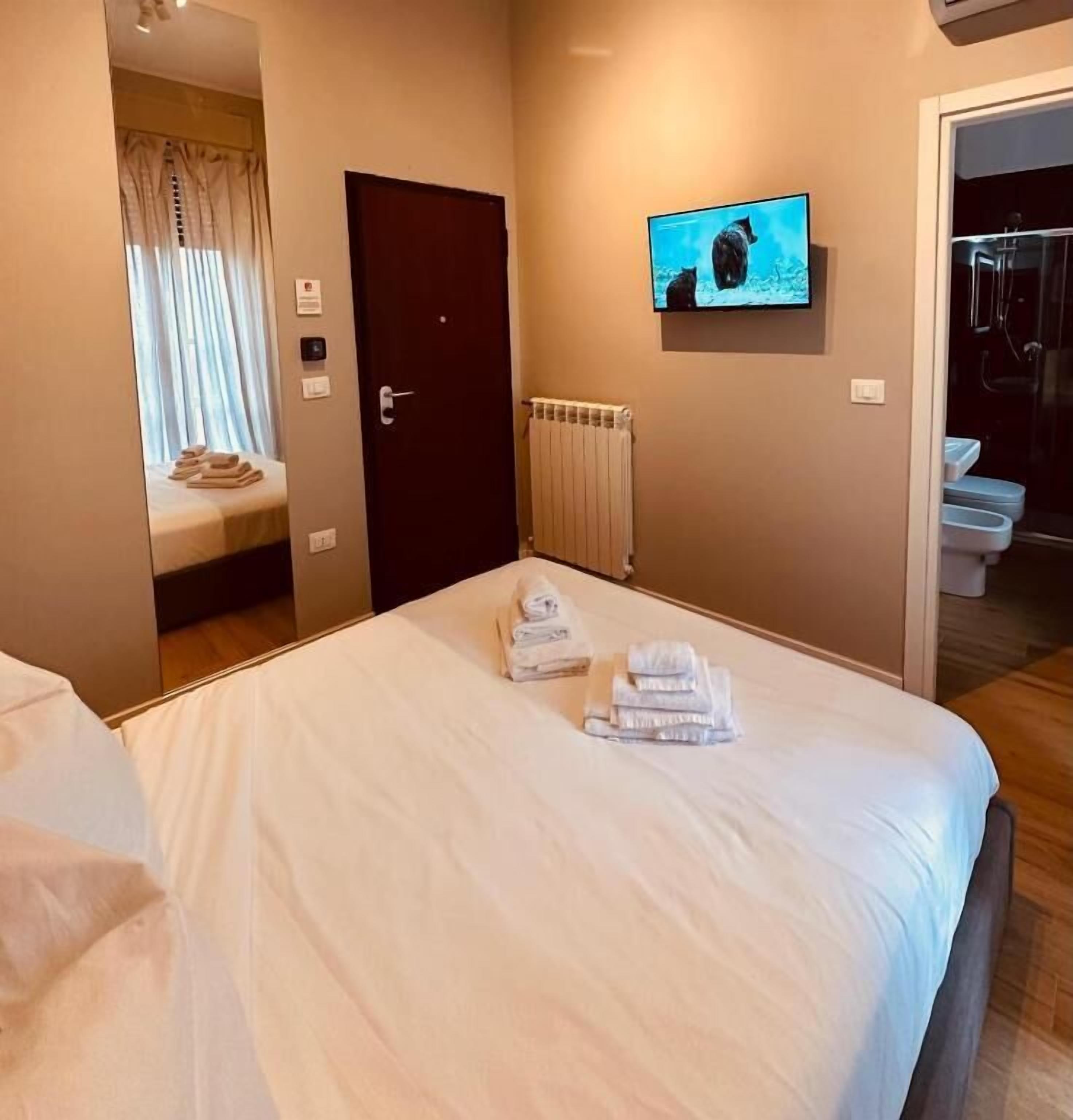 Ein Hotelzimmer mit Bett, einem an der Wand montierten Fernseher, einer Tür und Blick ins Badezimmer.