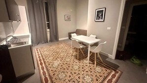 A compact living space with a kitchenette, a dining area with a table and chairs, a patterned rug, and a door leading to another room. - HH Tortona (Tortona)