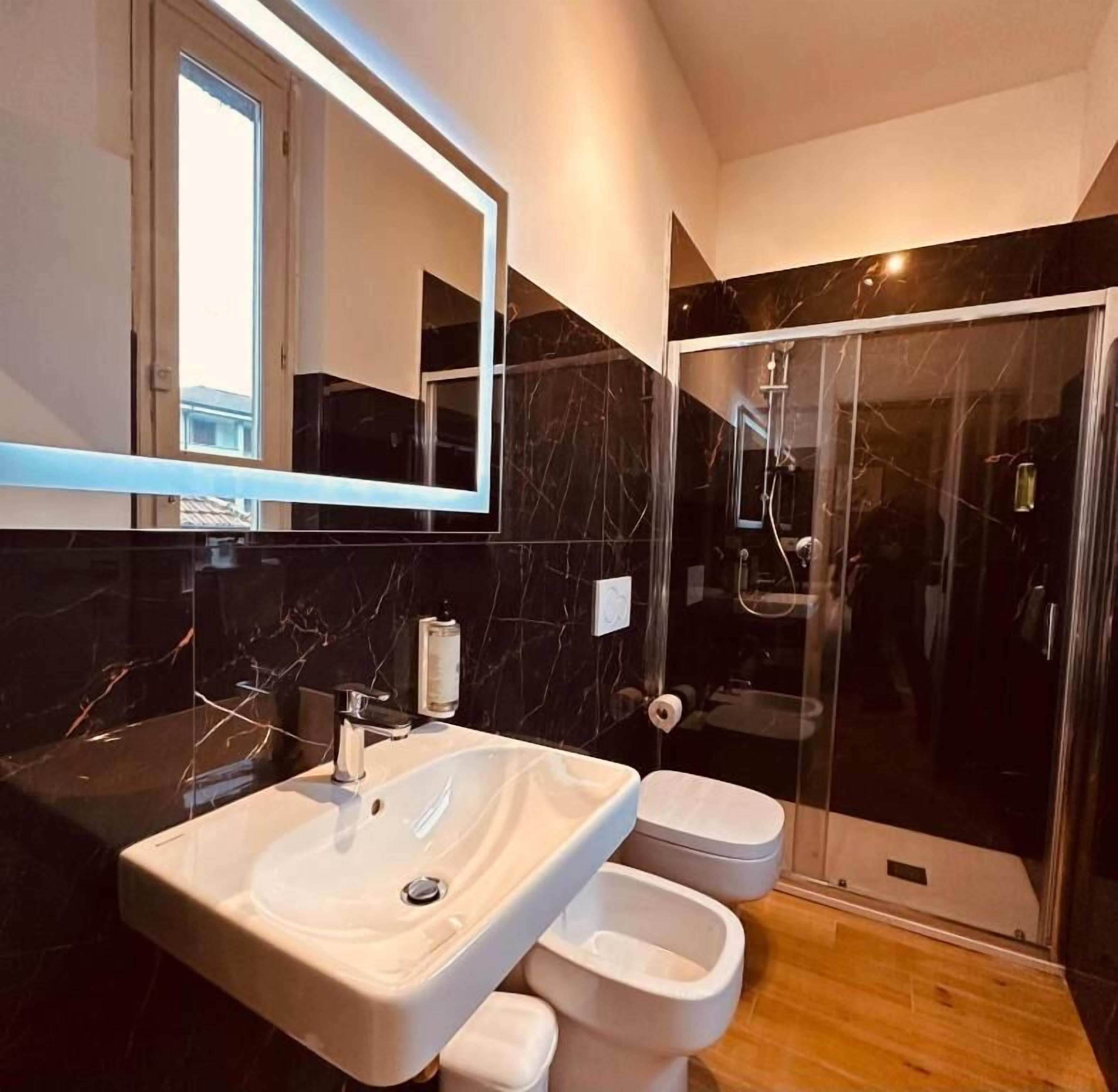 Un bagno moderno con un ampio specchio, un lavandino, due servizi igienici e una cabina doccia in vetro.
