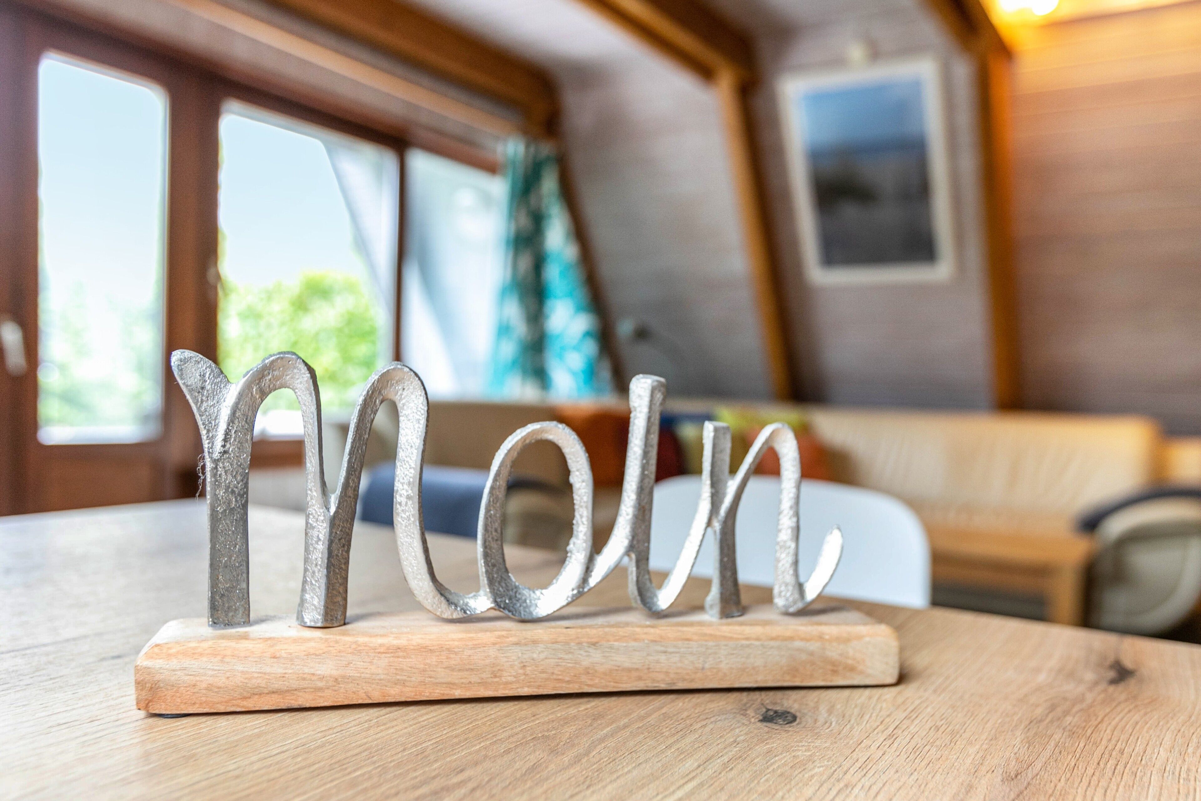 A metal sculpture on a wooden base in a room with a wooden ceiling, a window, and a framed picture on the wall.