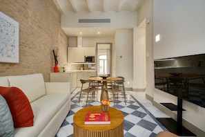 Een moderne woonkamer met een bank, een salontafel met een boek, een eethoek met stoelen, en een keuken op de achtergrond.