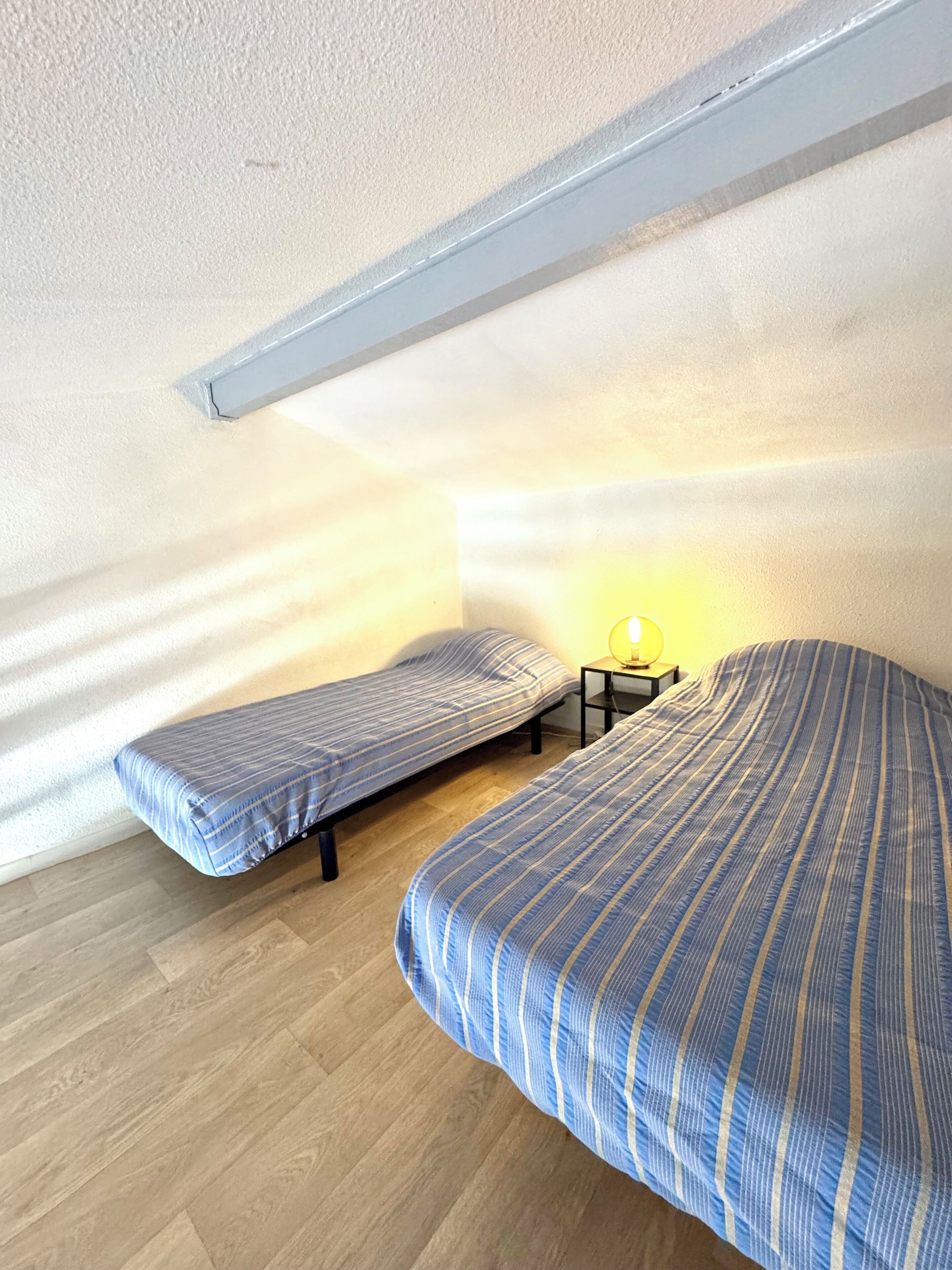 Een kleine kamer met twee bedden, een nachtkastje en een lamp.