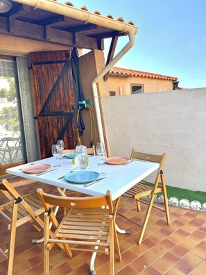 An outdoor dining area with a table set for two, wooden chairs, and a pergola overhead. - Micro house by the sea (Le Barcarès)