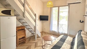 A bedroom with a bed, a television, a staircase, a refrigerator, and a window. - Micro house by the sea (Le Barcarès)