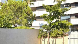 An outdoor dining area with a table set for two, surrounded by greenery and a modern building in the background. - Micro house by the sea (Le Barcarès)