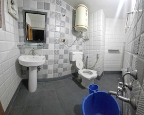 A bathroom with a white sink, toilet, and a blue bucket. - Hospitality Home  (Srinagar)